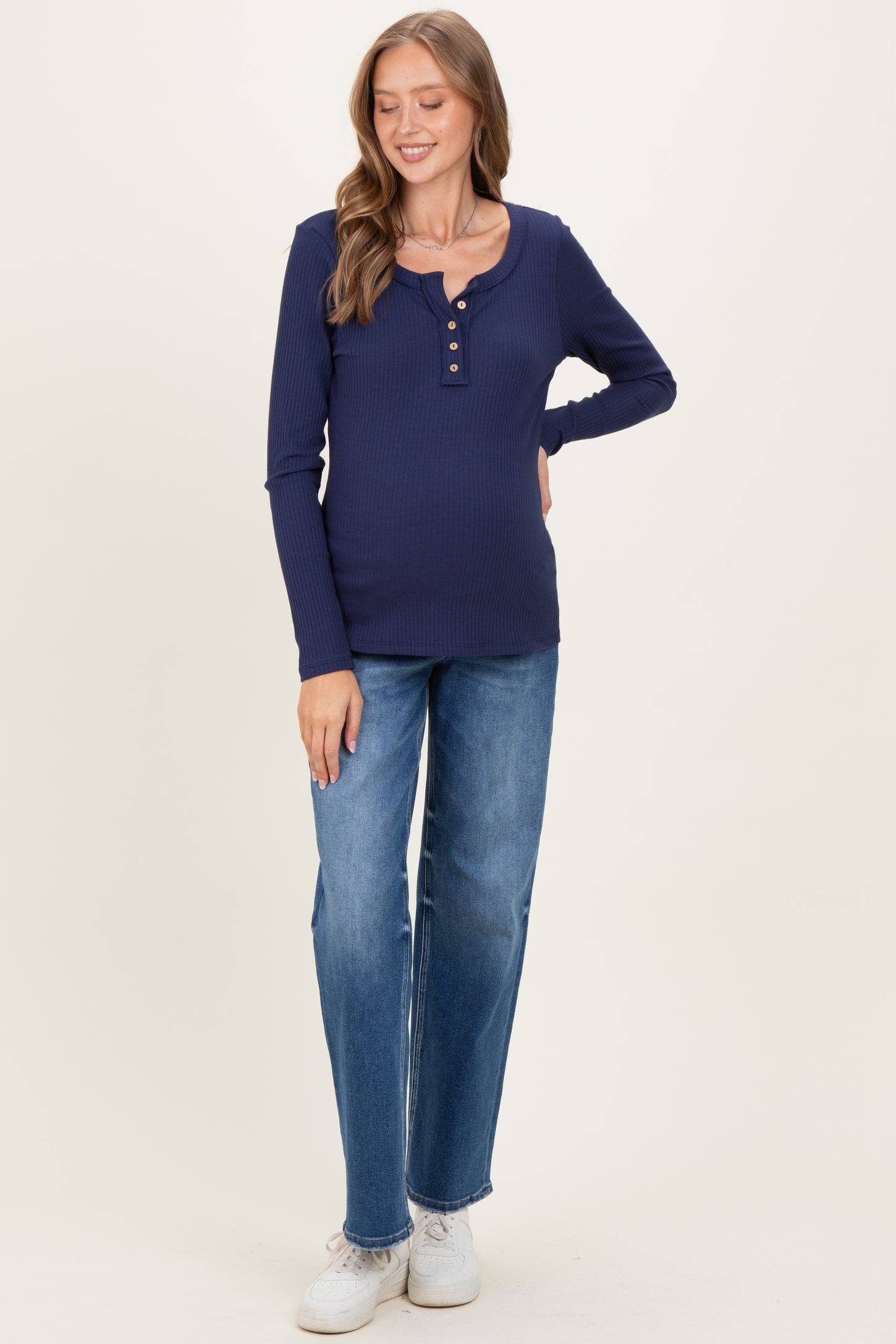 woman wearing a navy blue long sleeve maternity top with buttons and light blue jeans, showing her baby bump