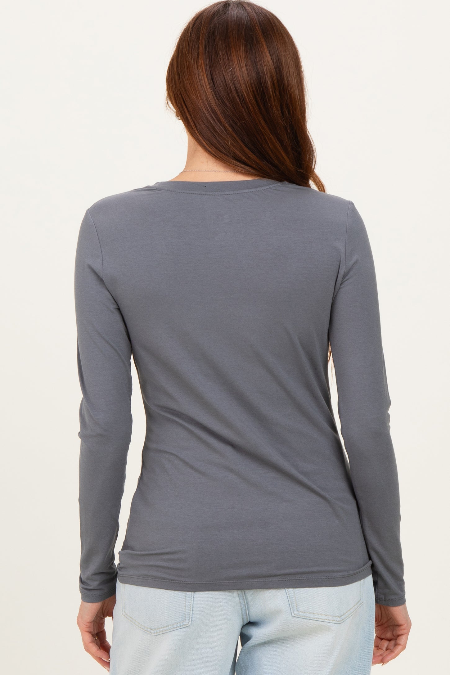 woman wearing a gray long sleeve top viewed from the back, styled with light blue jeans