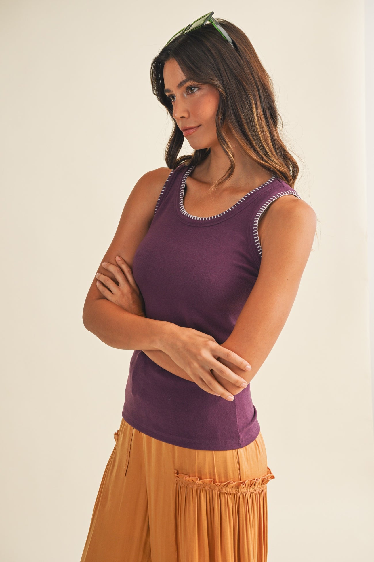 woman wearing a purple sleeveless top with contrasting trim and orange flowy pants, standing with arms crossed