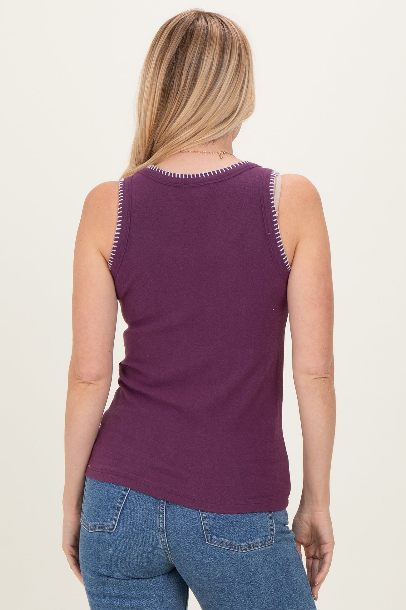 woman wearing a purple sleeveless top with contrasting trim and blue jeans, viewed from the back
