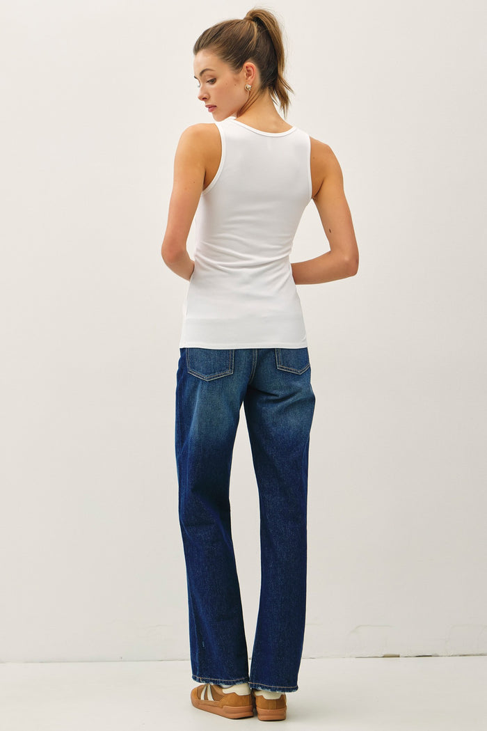 woman wearing a white sleeveless top and high-waisted blue denim jeans, viewed from the back