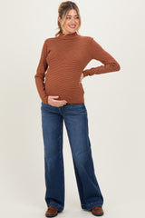 woman wearing a rust striped maternity long sleeve top and blue flared jeans, holding her baby bump