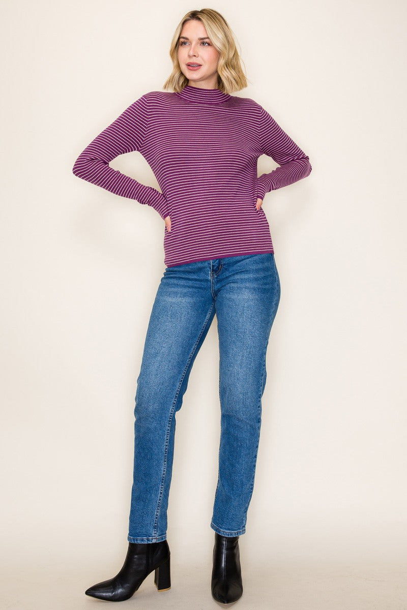 woman wearing a purple and striped long sleeve top with fitted sleeves and blue jeans, paired with black ankle boots