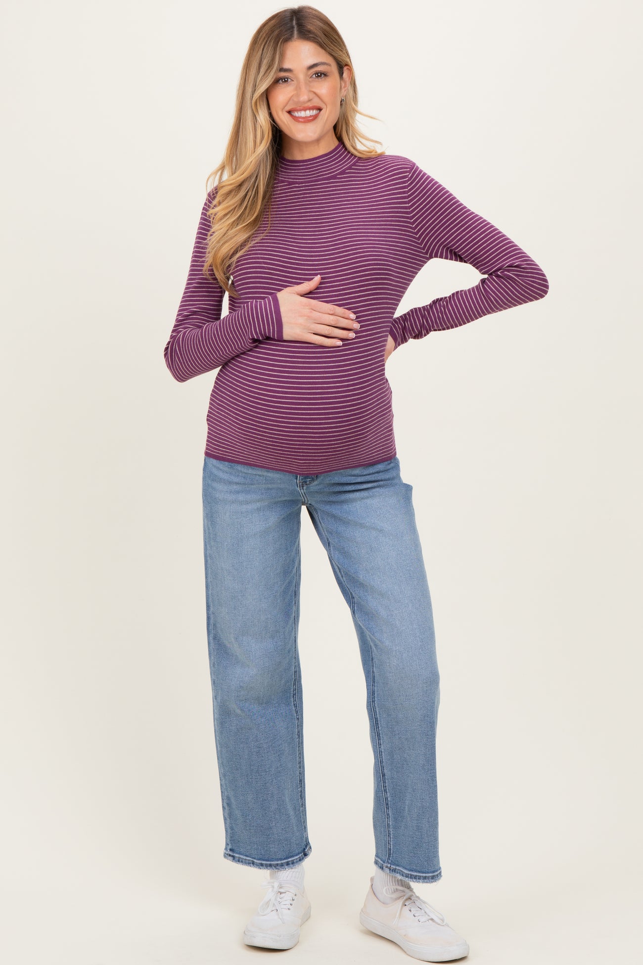 woman wearing a purple striped maternity top and blue jeans, holding her baby bump