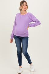 woman wearing a lavender maternity sweatshirt with a round neckline and relaxed fit, paired with skinny jeans and white sneakers