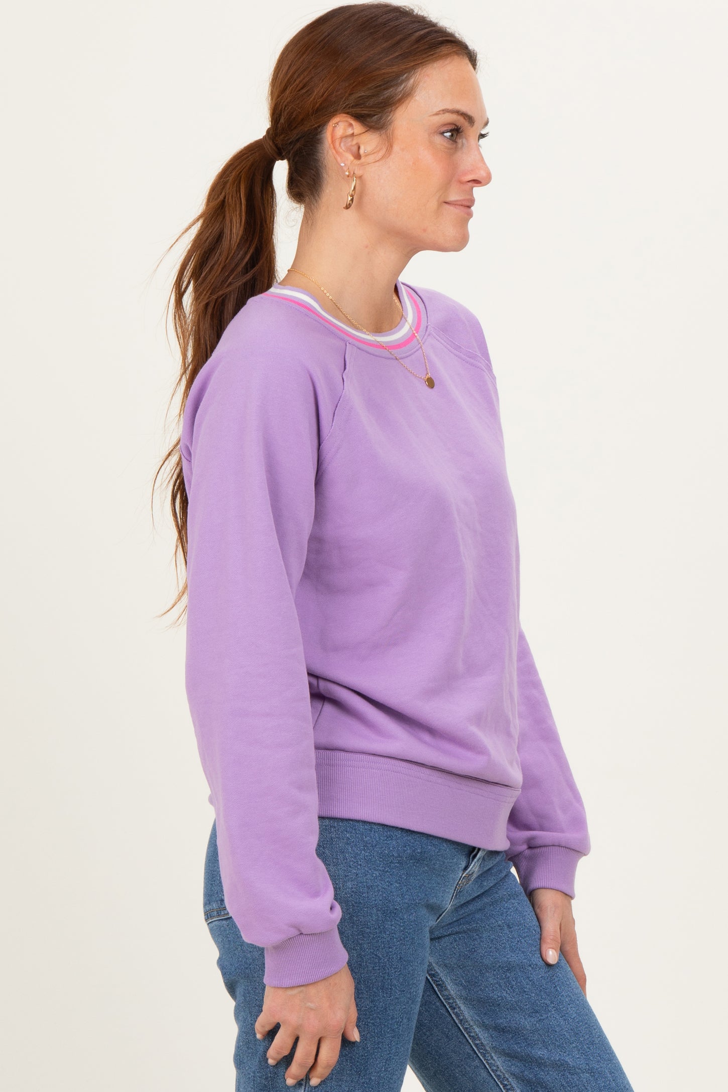 woman wearing a purple sweatshirt with contrasting neckline and side stripes, paired with blue jeans