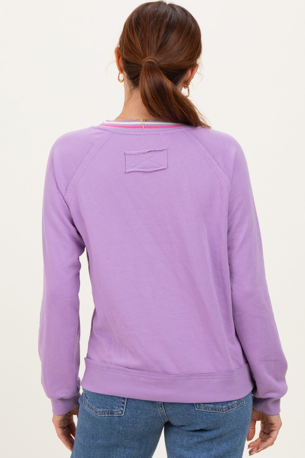 woman wearing a lavender long sleeve sweatshirt with a relaxed fit and back logo detail, styled with jeans