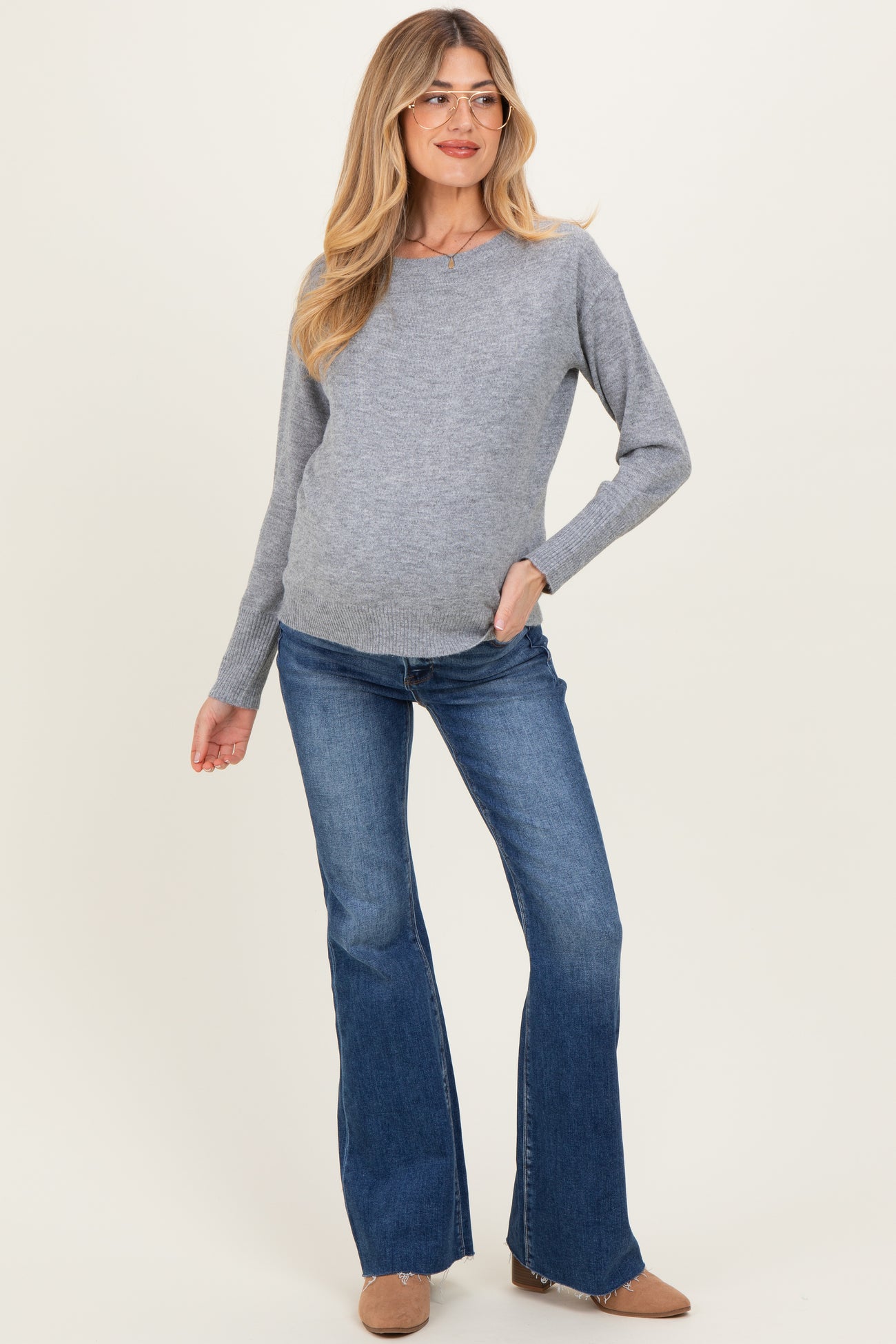 woman wearing a gray maternity sweater with a v-neck and blue flared jeans, showing her baby bump