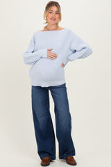 woman wearing a light blue maternity sweater with loose fit and holding her baby bump, paired with flared jeans