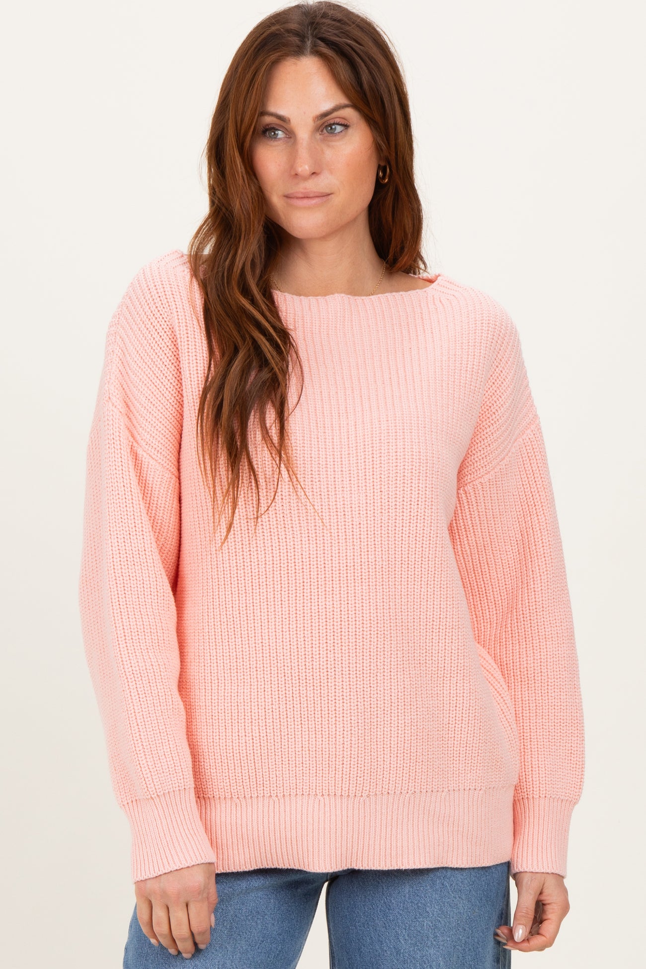woman wearing a soft pink oversized knit sweater with a wide neckline and ribbed texture, styled with blue jeans