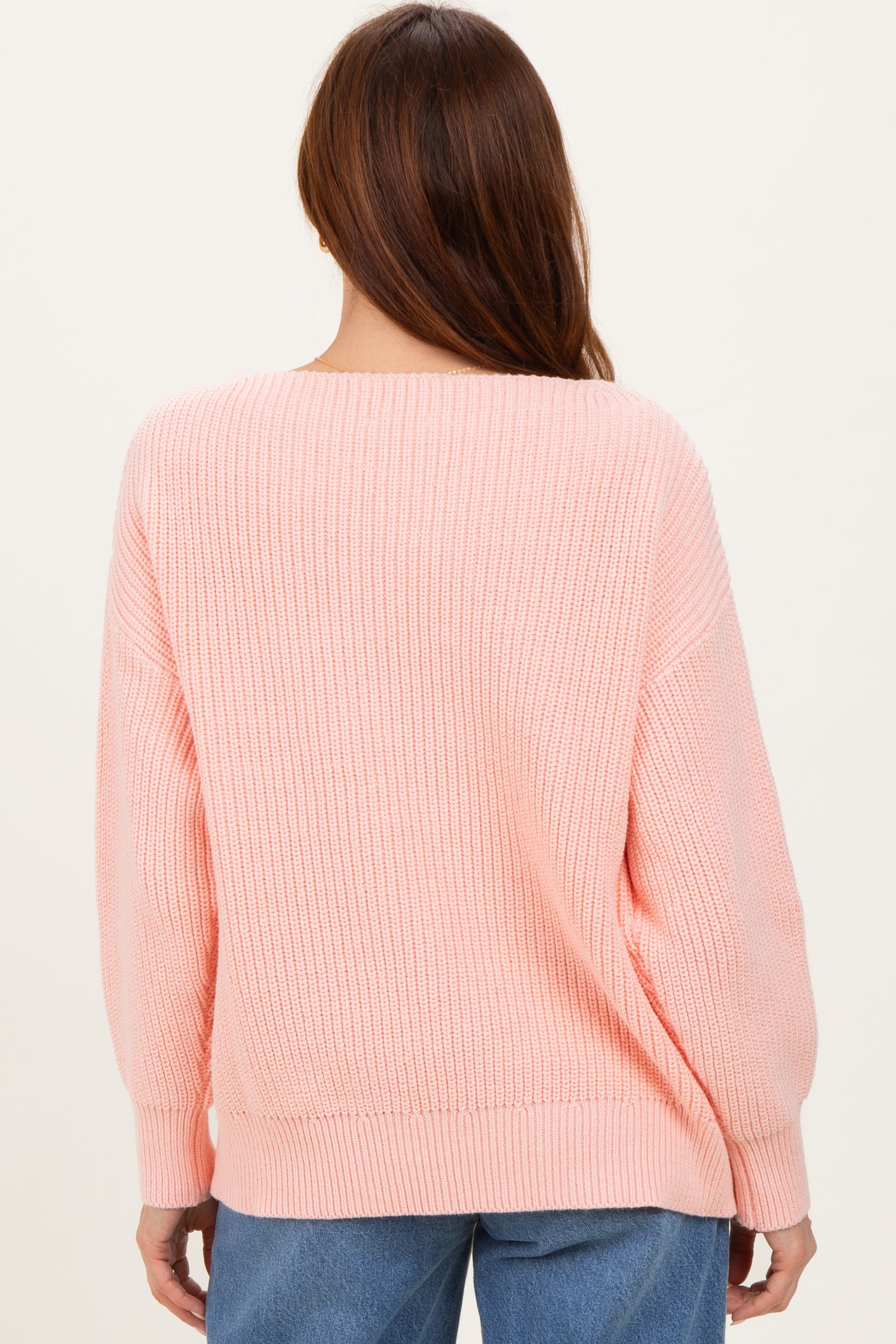 woman wearing a soft pink oversized knit sweater from the back, styled with relaxed-fit denim jeans