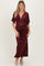 woman wearing a burgundy floral velvet maternity gown with short flutter sleeves and a deep v-neckline, showing her baby bump