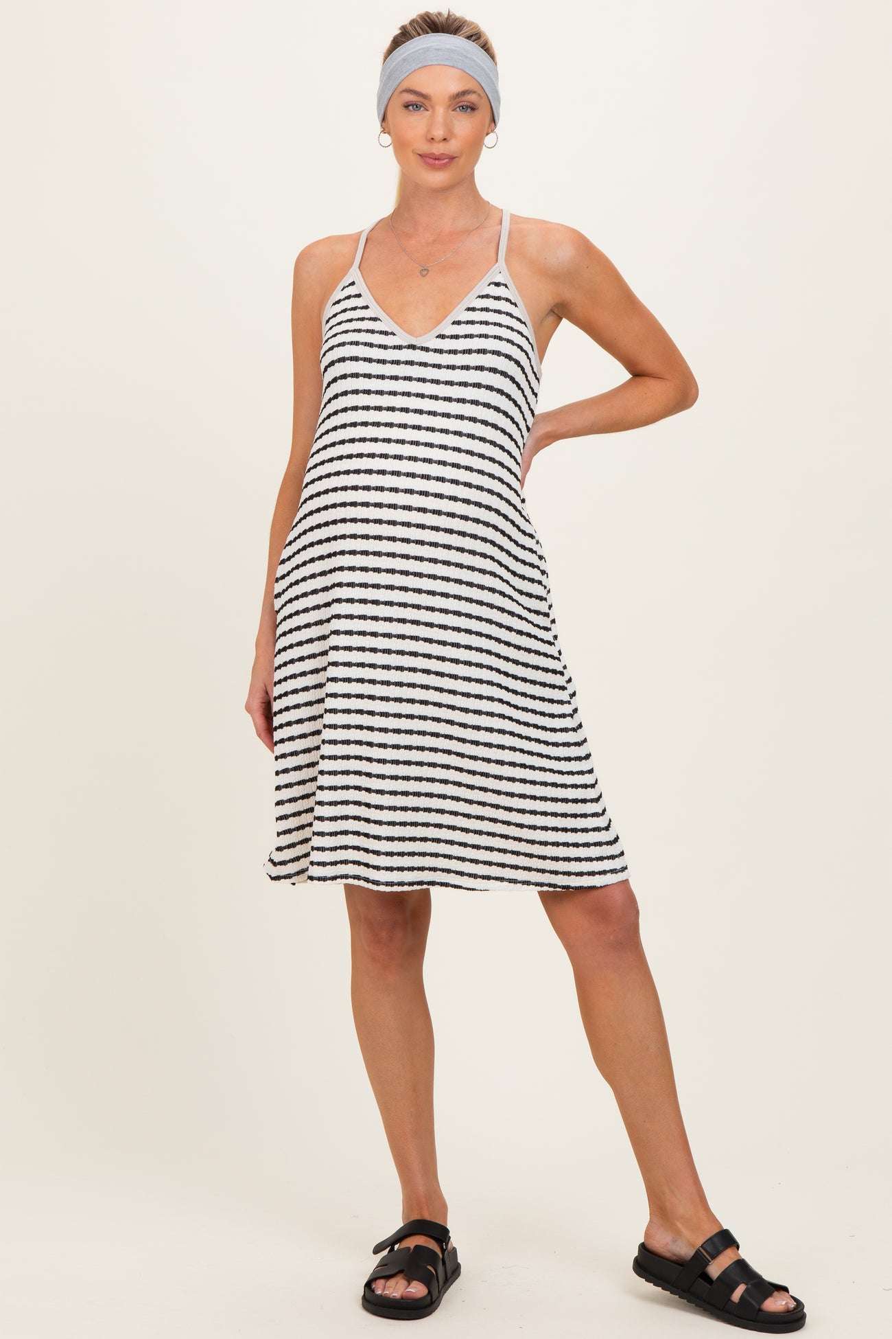 woman wearing a black and white striped maternity dress with a v-neckline and a flowy skirt, posing with one hand on her hip