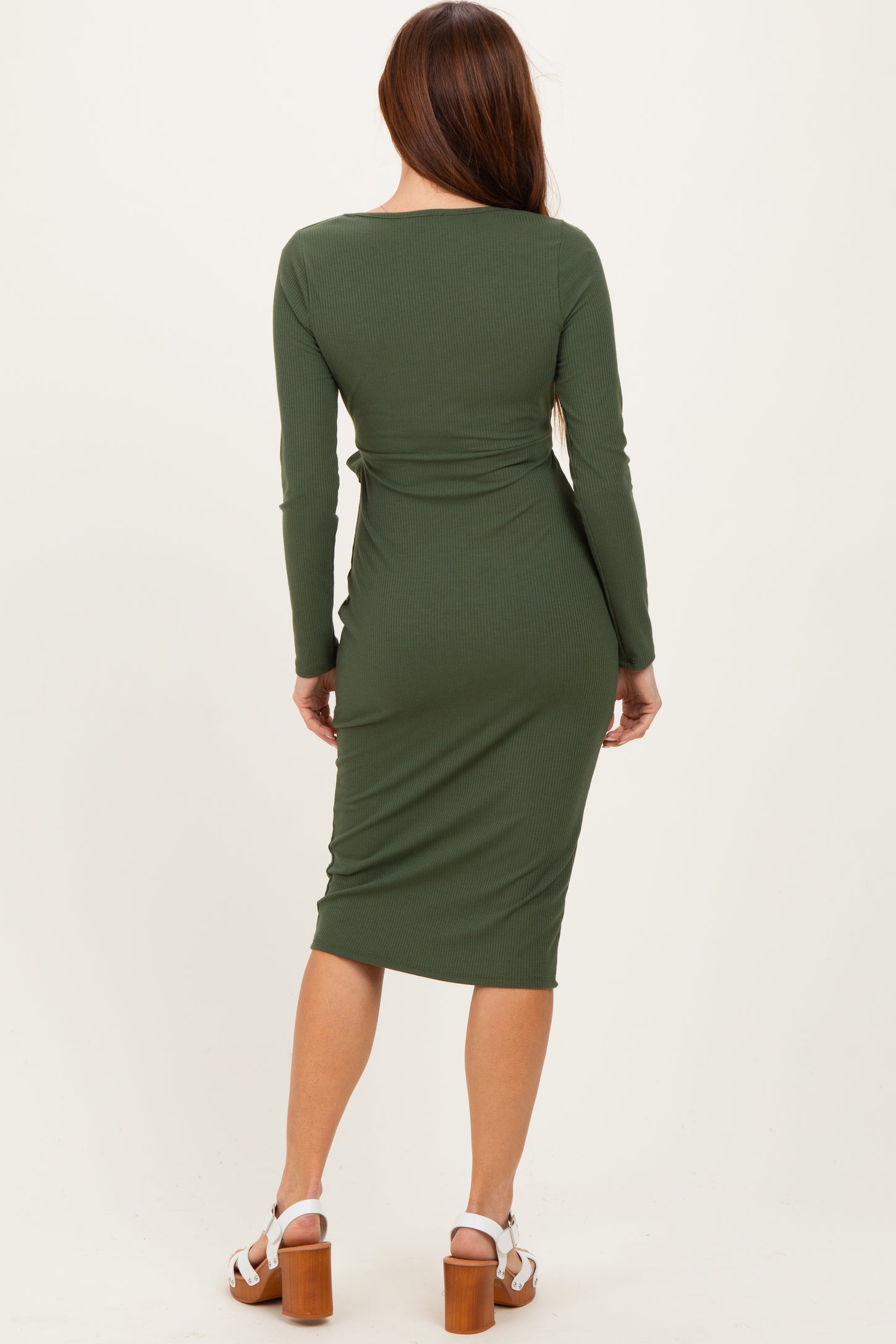 woman wearing a fitted olive green long sleeve midi dress with a ruched detail at the back and high heels