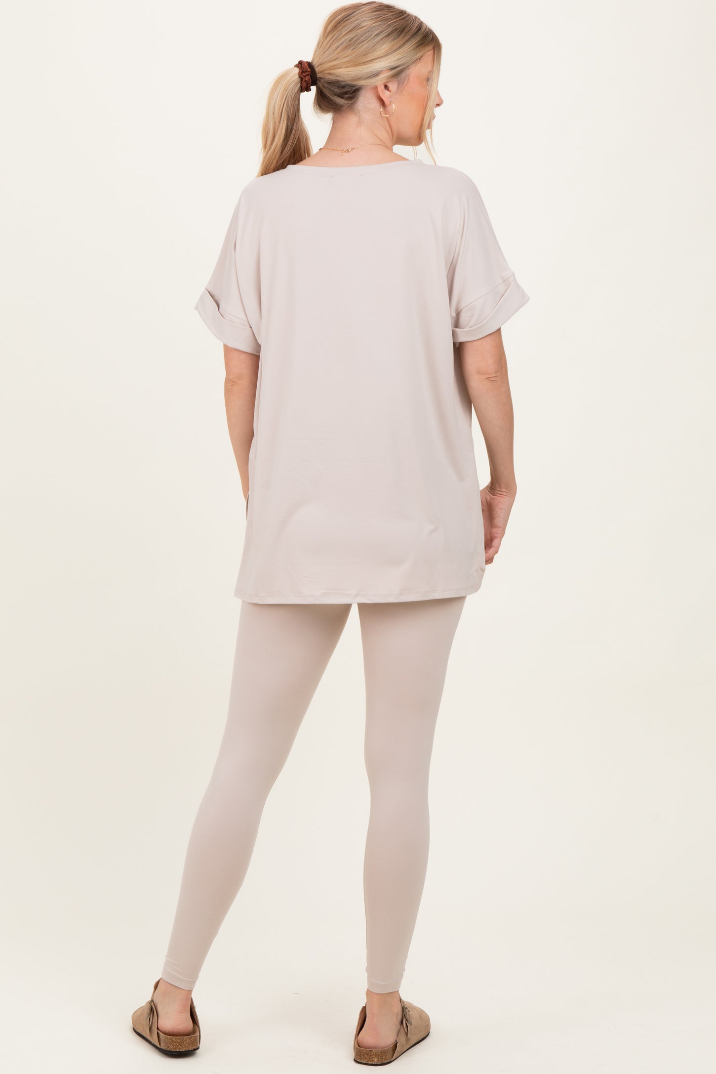 woman wearing a light beige oversized t-shirt and matching beige leggings, standing with her back to the camera