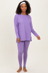 woman wearing a purple long sleeve top and matching leggings, standing with a smile