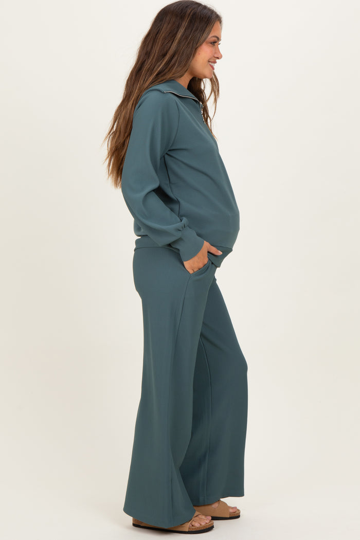 woman wearing a slate blue maternity loungewear set with a hooded top and wide-leg pants, showing her baby bump