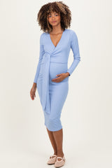woman wearing a light blue long sleeve maternity dress with a wrap design and holding her baby bump