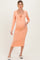 woman wearing a coral long sleeve maternity dress with a square neckline and tie detail, showing her baby bump
