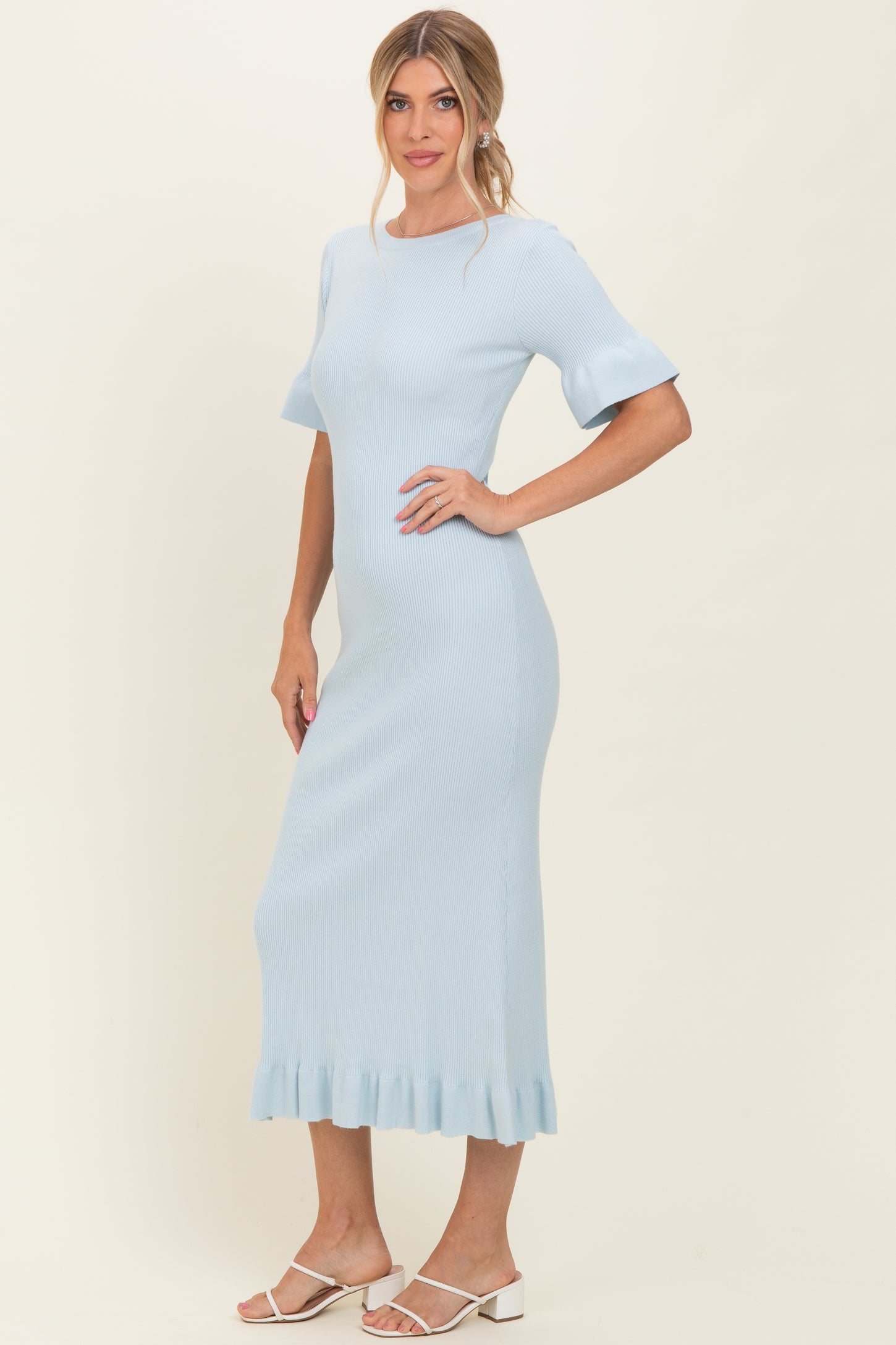 woman wearing a light blue ribbed midi dress with flared sleeves and a ruffled hem, standing against a neutral background