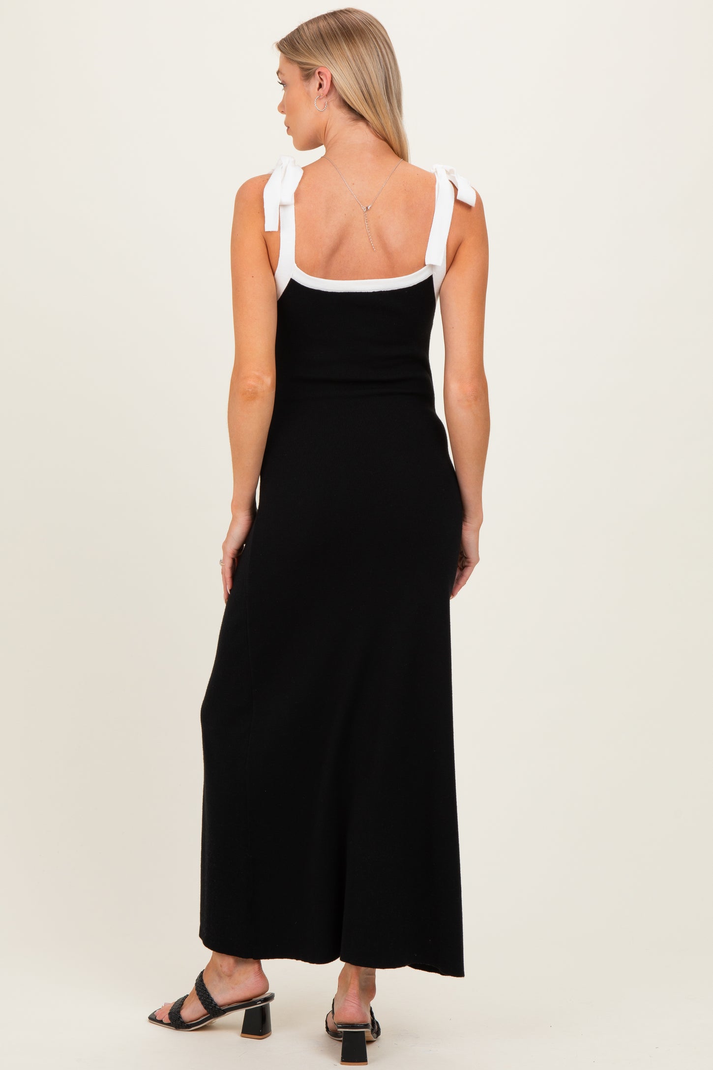 woman wearing a black maternity maxi dress with white bow shoulder straps and a fitted silhouette