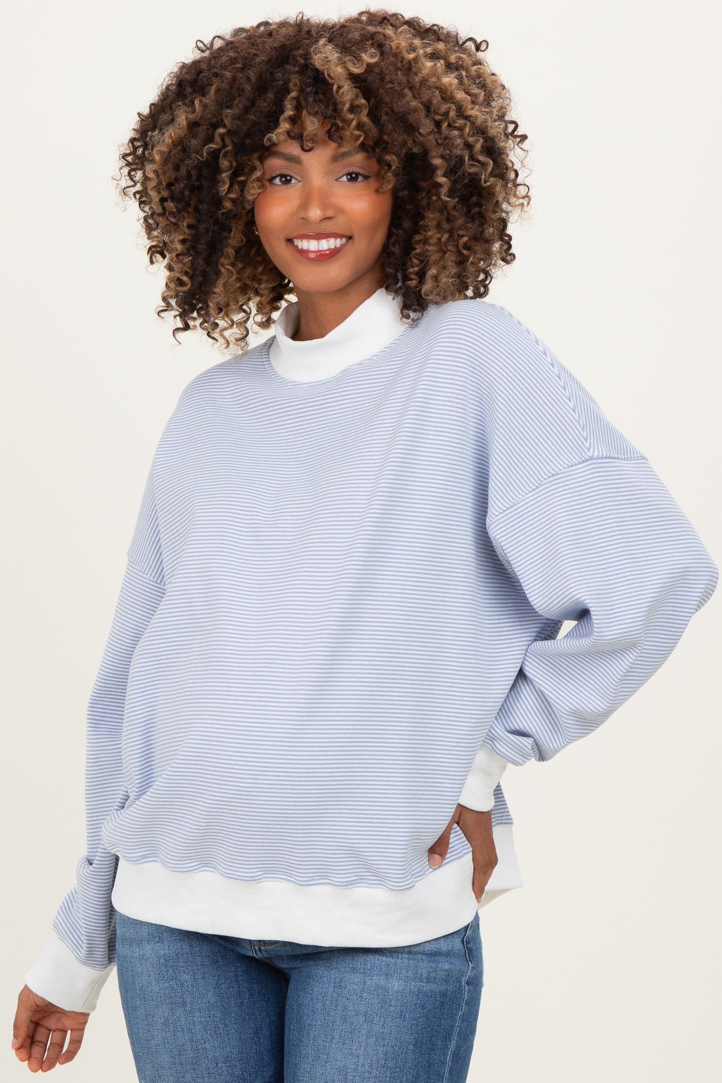 woman wearing a light blue striped maternity sweatshirt with white accents and denim jeans, showing her baby bump