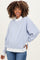 woman wearing a light blue striped maternity sweatshirt with white accents and denim jeans, showing her baby bump