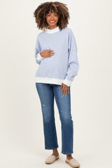 woman wearing a light blue maternity long sleeve sweatshirt with a white mock neck and holding her baby bump, paired with jeans