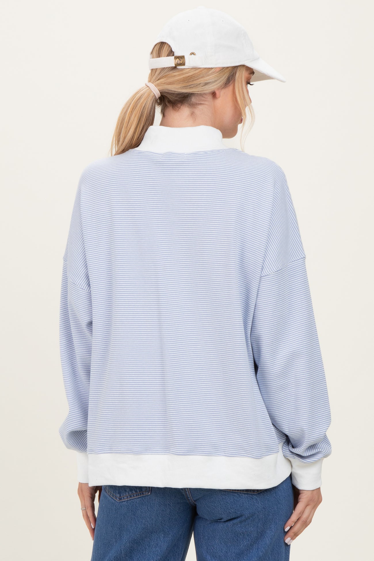 woman wearing a light blue striped long sleeve sweatshirt with a white trim and a white cap, viewed from the back