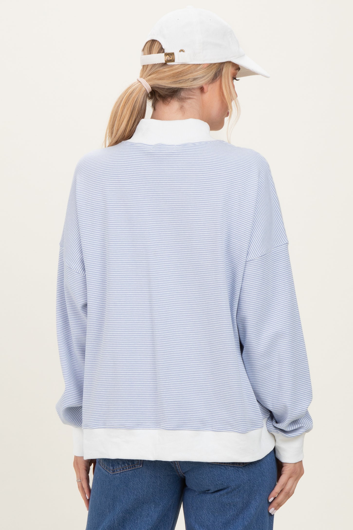 woman wearing a light blue striped long sleeve sweatshirt with a white trim and a white cap, viewed from the back