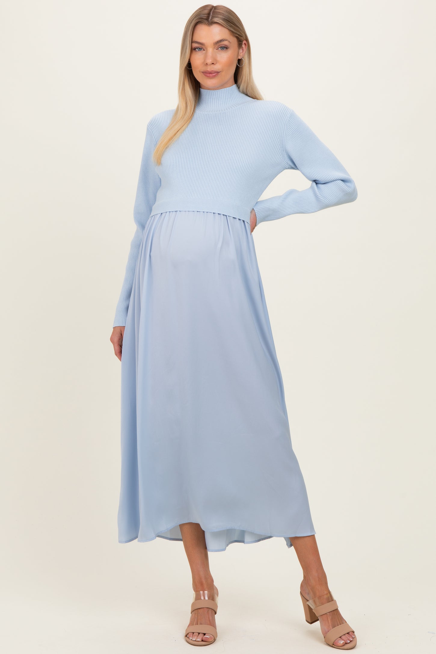 woman wearing a light blue maternity dress with a ribbed sweater top and flowy skirt, showcasing her baby bump