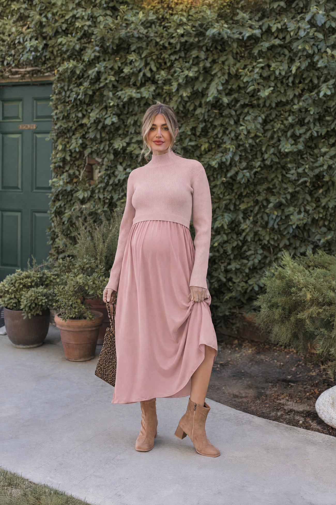 woman wearing a light pink long sleeve maternity dress with a ruffled hem and a visible baby bump