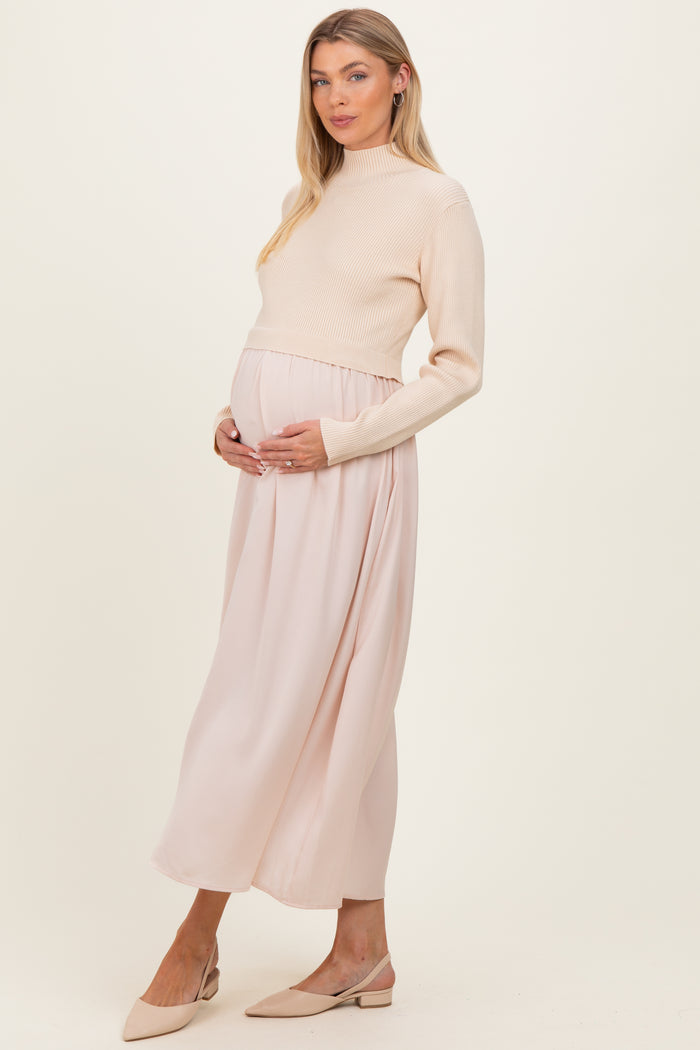 woman wearing a cream ribbed maternity sweater and a flowing blush pink maternity maxi skirt, holding her baby bump