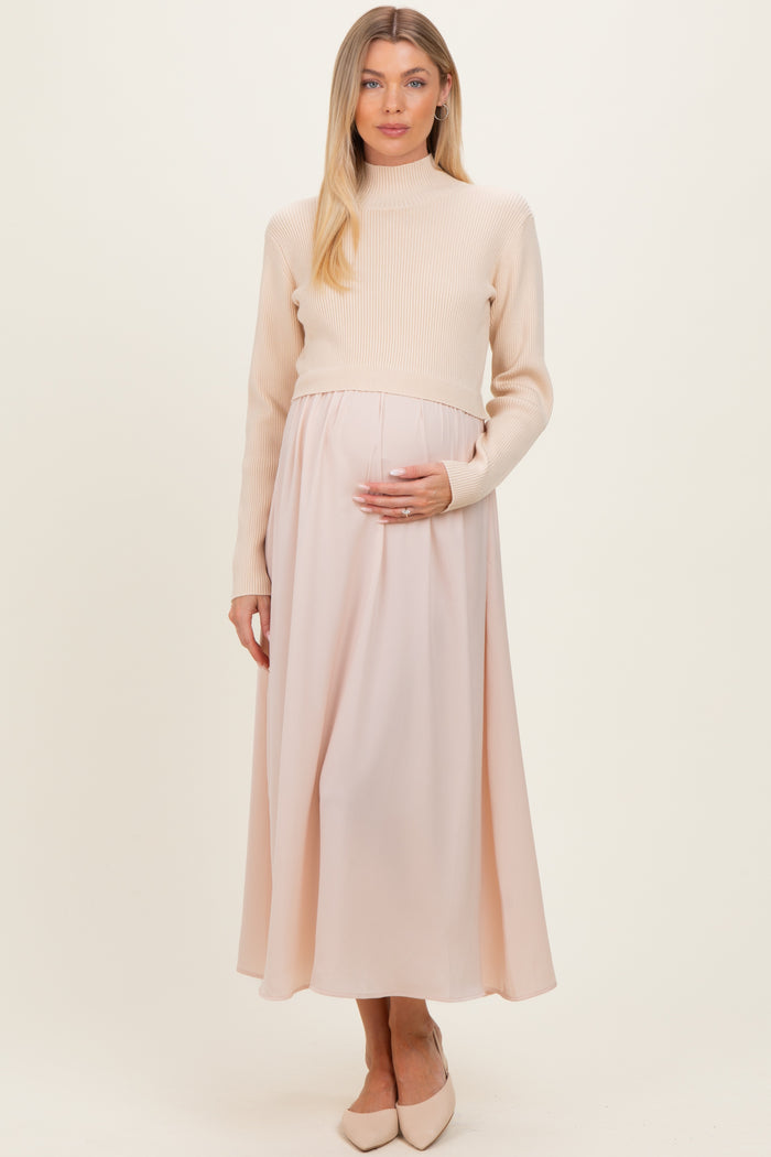 woman wearing a cream ribbed maternity sweater and a pale pink maxi skirt, gently holding her baby bump