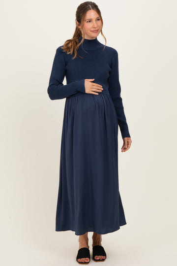 woman wearing a navy blue long sleeve maternity dress with a fitted top and flowing skirt, holding her baby bump