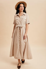 woman wearing a beige striped button-up maxi dress with a tie waist and short sleeves, paired with a hat and flats