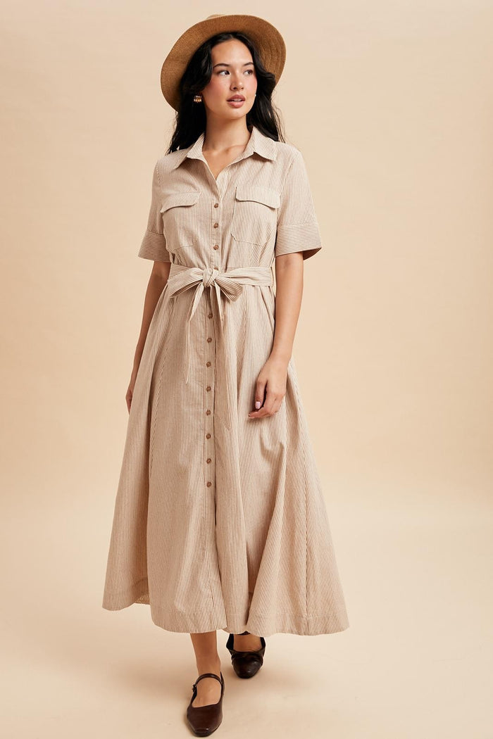woman wearing a beige striped button-up maxi dress with a tie waist and short sleeves, paired with a hat and flats