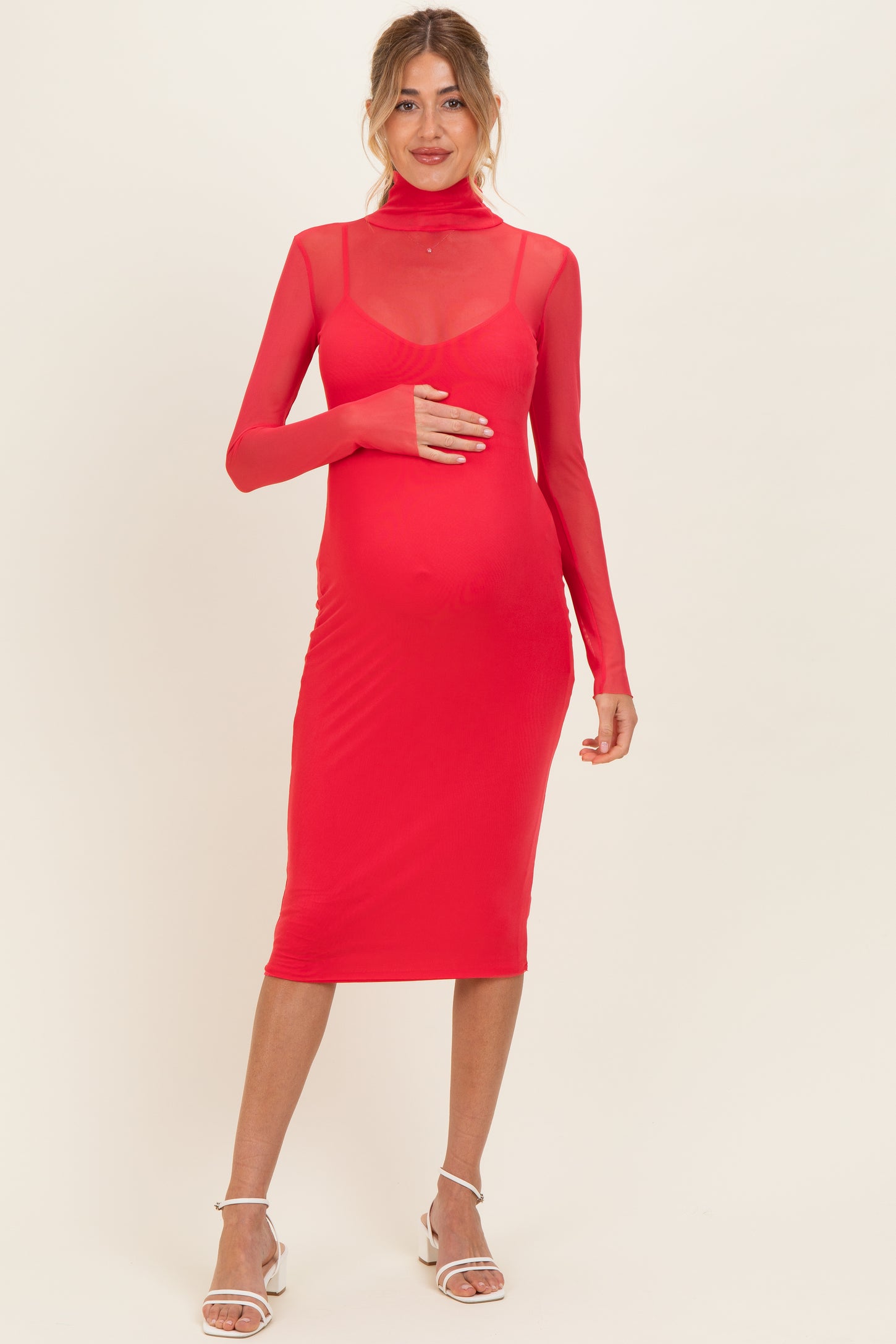 woman wearing a red maternity dress with a sheer turtleneck and long sleeves, holding her baby bump