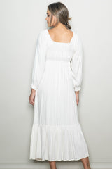 woman wearing a white long sleeve maxi dress with a fitted bodice and ruffled hem, view from the back