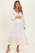 woman wearing a white long sleeve maternity dress with a ruffled hem and buttons, holding her baby bump