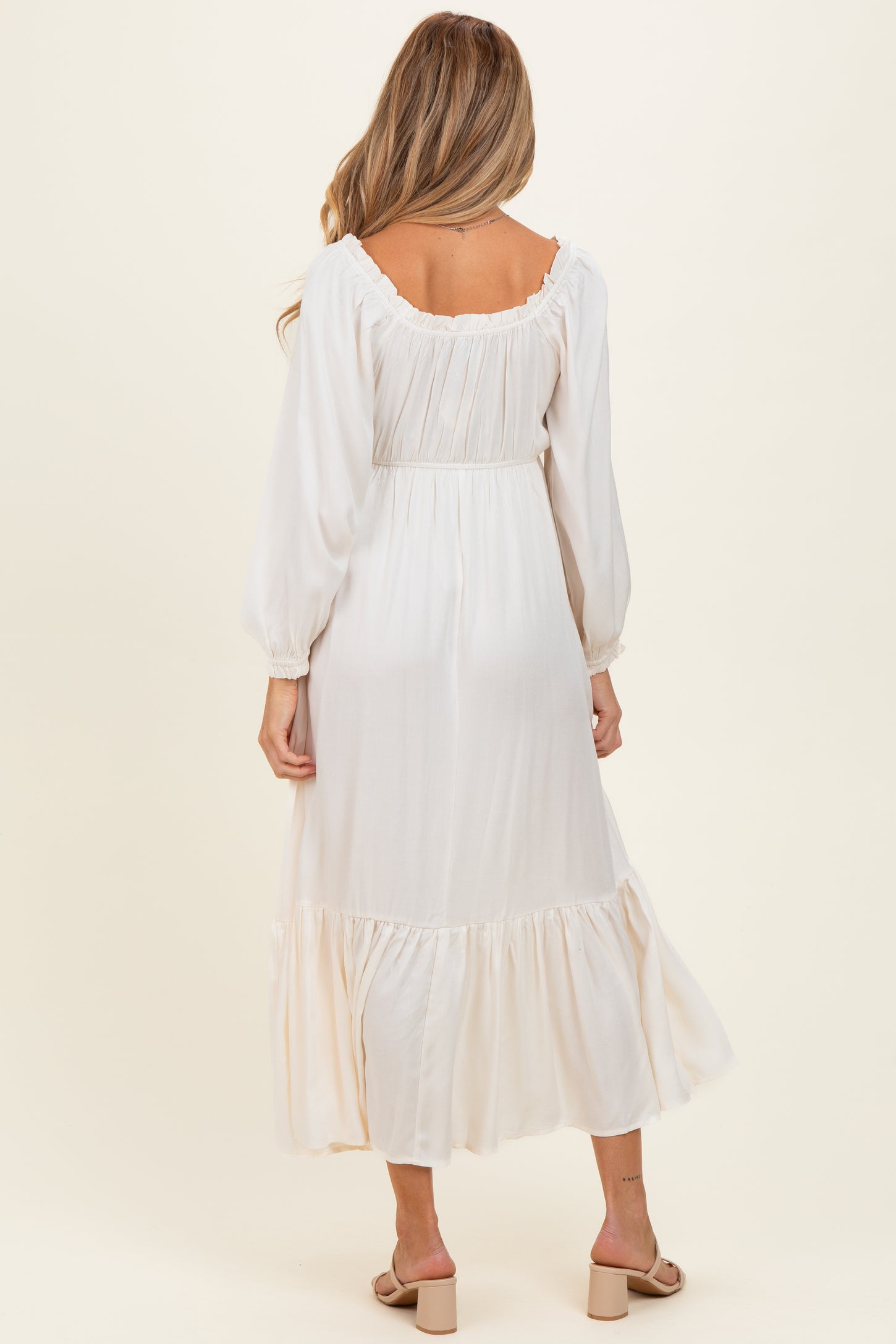woman wearing a cream long sleeve maternity maxi dress with ruffle details and a cinched waist