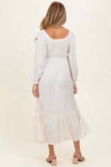 woman wearing a cream long sleeve maternity maxi dress with ruffle details and a cinched waist