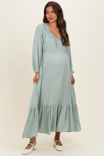 woman wearing a sage green long sleeve maternity dress with button details and a tiered skirt, showcasing her baby bump