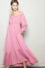 woman wearing a pink off-shoulder maxi dress with button details and ruffled hem, posing with one hand in pocket