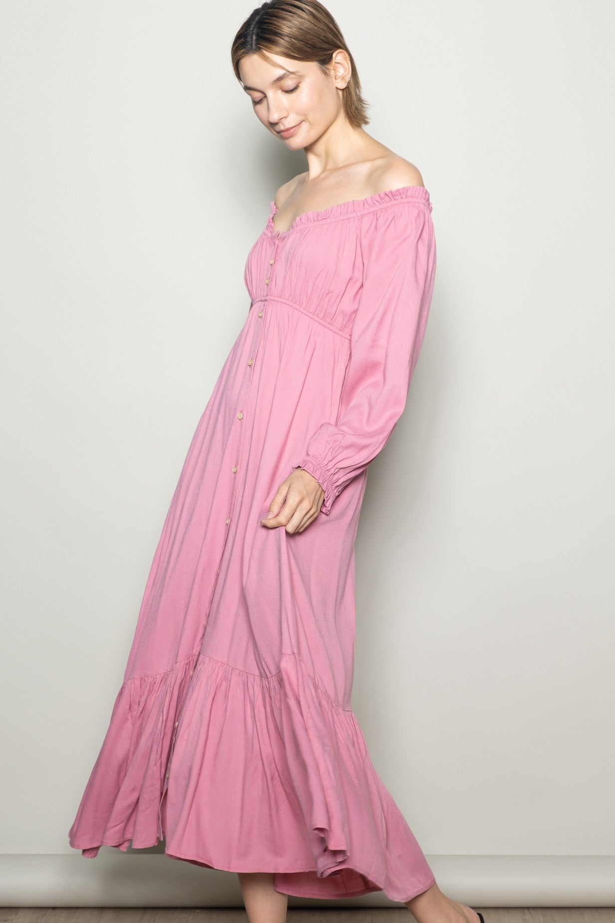 woman wearing a pink off-the-shoulder maxi dress with a button-down front and long sleeves.