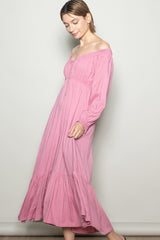 woman wearing a pink off-the-shoulder maxi dress with a button-down front and long sleeves.