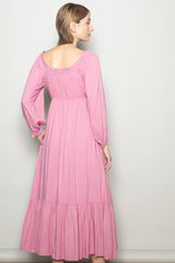 woman wearing a pink long sleeve maxi dress with a smocked back and tiered hem, standing with her back to the camera