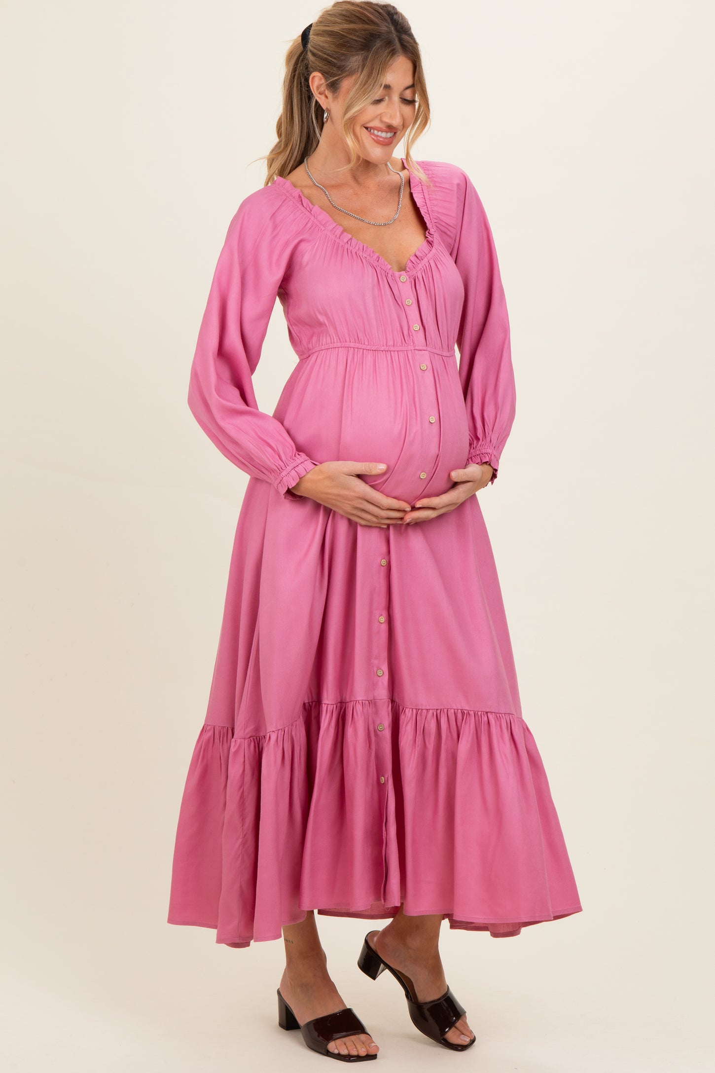 woman wearing a pink maternity maxi dress with buttons and ruffled hem, showing her baby bump