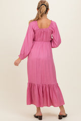 woman wearing a pink long sleeve maternity dress with ruffle details and a tiered hem, showing her baby bump from the back