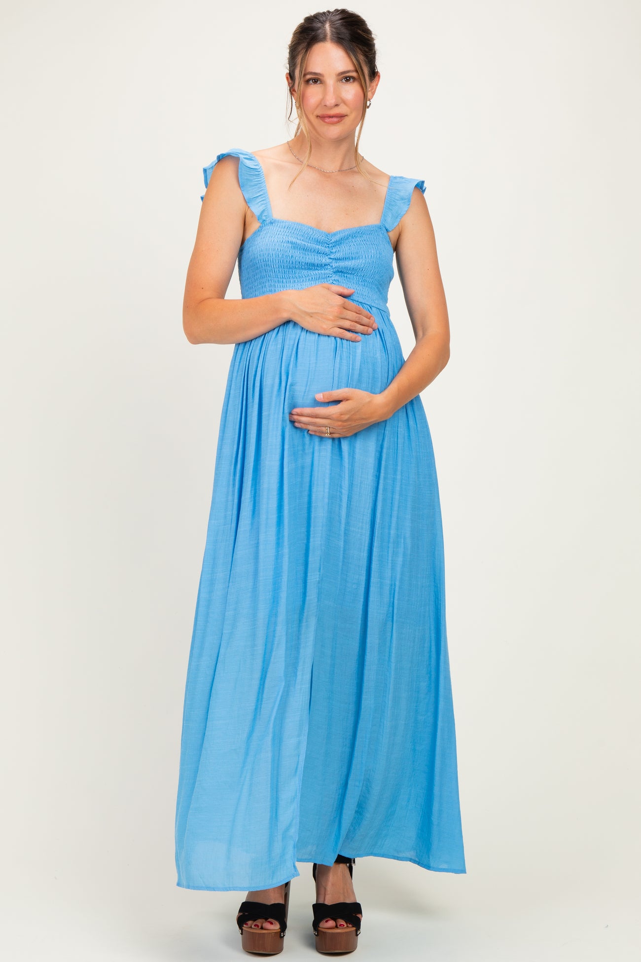 woman wearing a light blue maternity maxi dress with ruffled straps and holding her baby bump